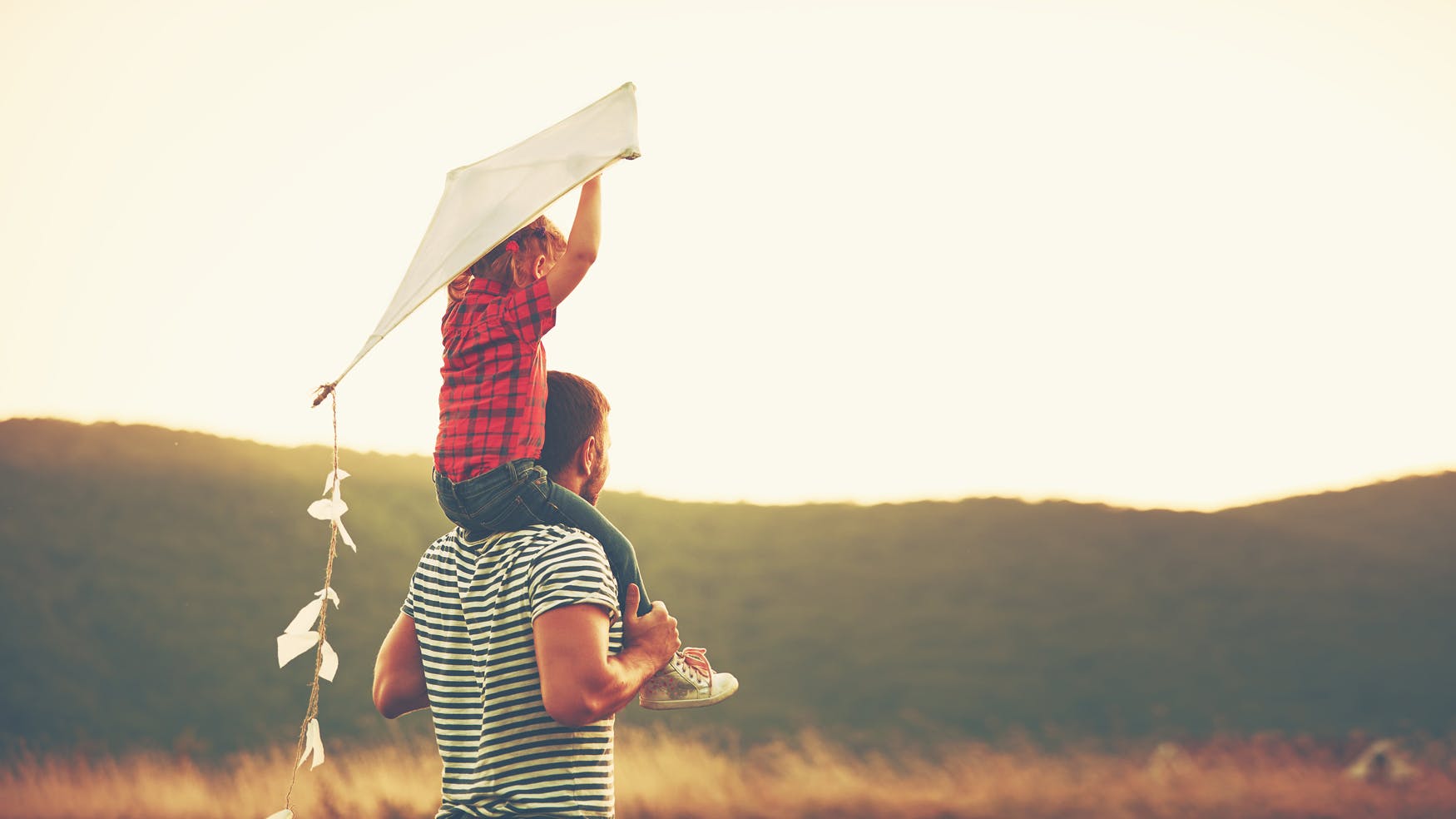 Father carries child on shoulders who is holding a kite
